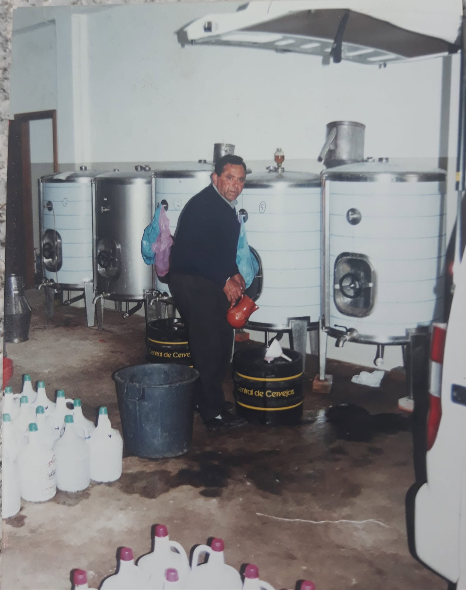 Fotografia antiga da adega, com as cubas de inox e garrafões de vinho